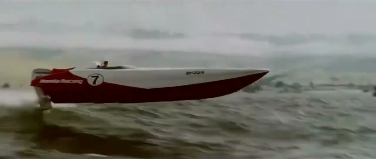 A red and white Honda Racing powerboat with number 7 on its side speeds across choppy water, creating a large spray, with a misty shoreline in the background.