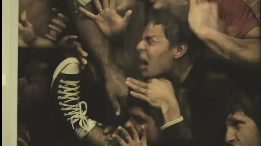 A crowd of men are pressed together, with one man's foot in a black and white sneaker visible, as they struggle and shout in a tight space.