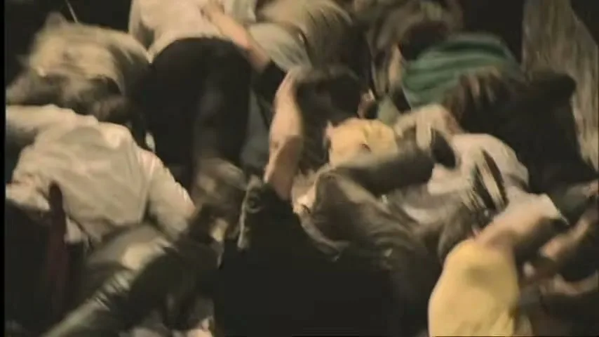 A man in a light shirt runs past an office window, revealing a chaotic pile of people climbing over each other outside.