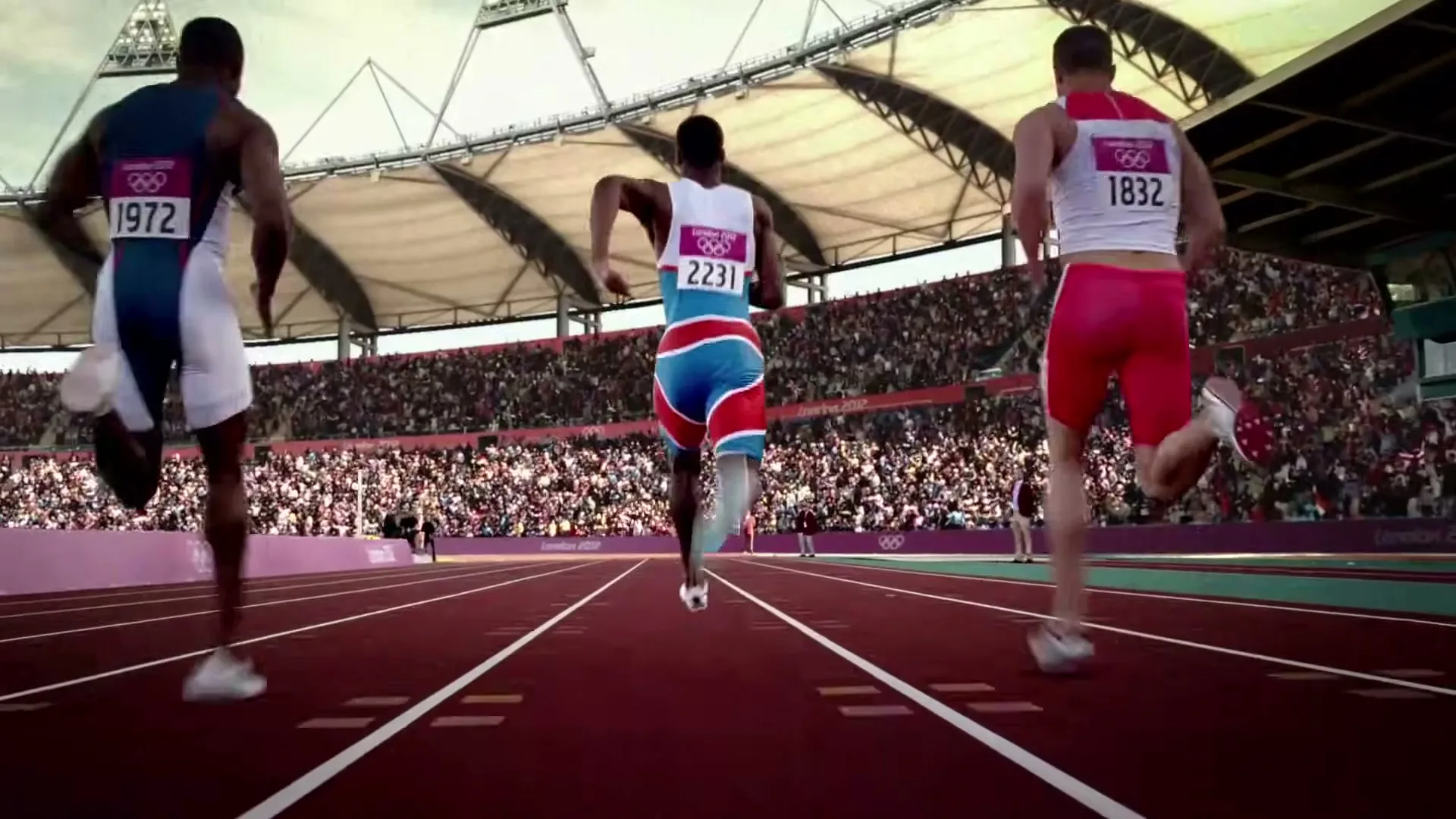 Three male athletes in running gear sprint on a track in a stadium full of spectators during the London 2012 Olympics.