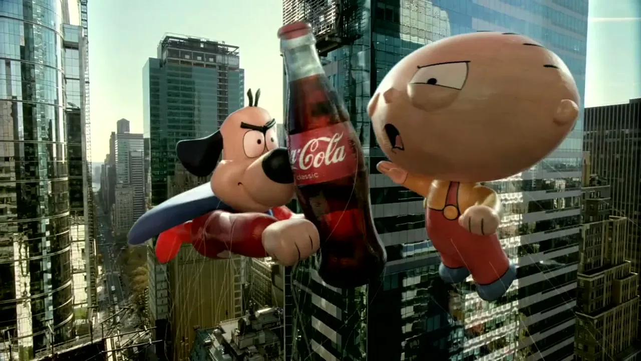 Two large cartoon character balloons, a dog and a baby, float high above a city street, fighting over a giant Coca-Cola bottle.