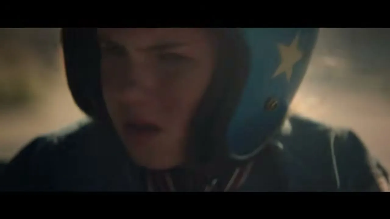 A young female racer, wearing a blue helmet with a yellow star, is focused and determined while riding a motorcycle on a dirt track.