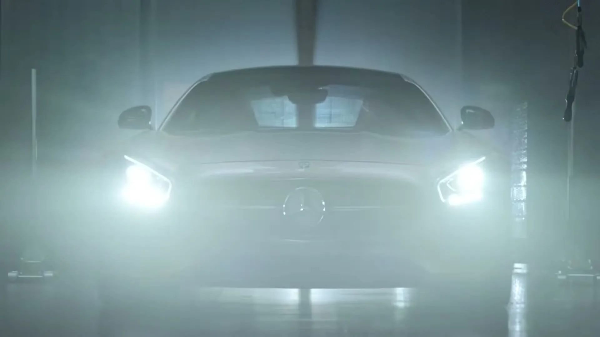 A silver Mercedes-Benz sports car with its headlights on is seen head-on in a dark, smoky garage.