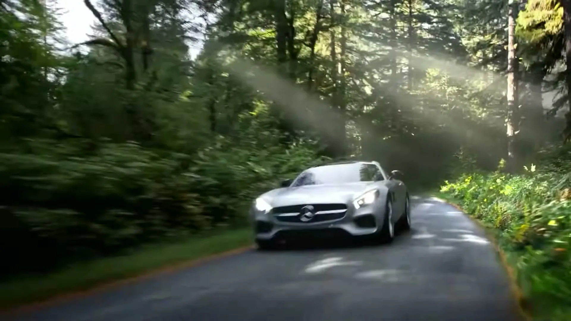 A silver Mercedes-Benz sports car drives quickly down a winding road through a sun-dappled forest, with light rays piercing through the trees.