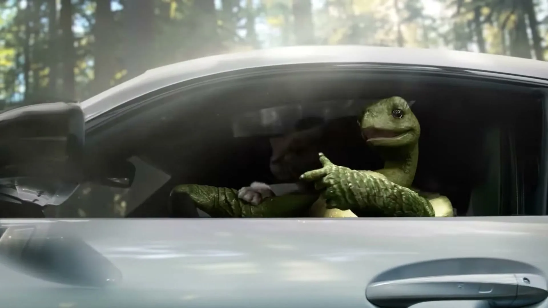 A CGI turtle and rabbit are seen inside a silver car, with the turtle in the passenger seat and the rabbit driving, in a forest setting.