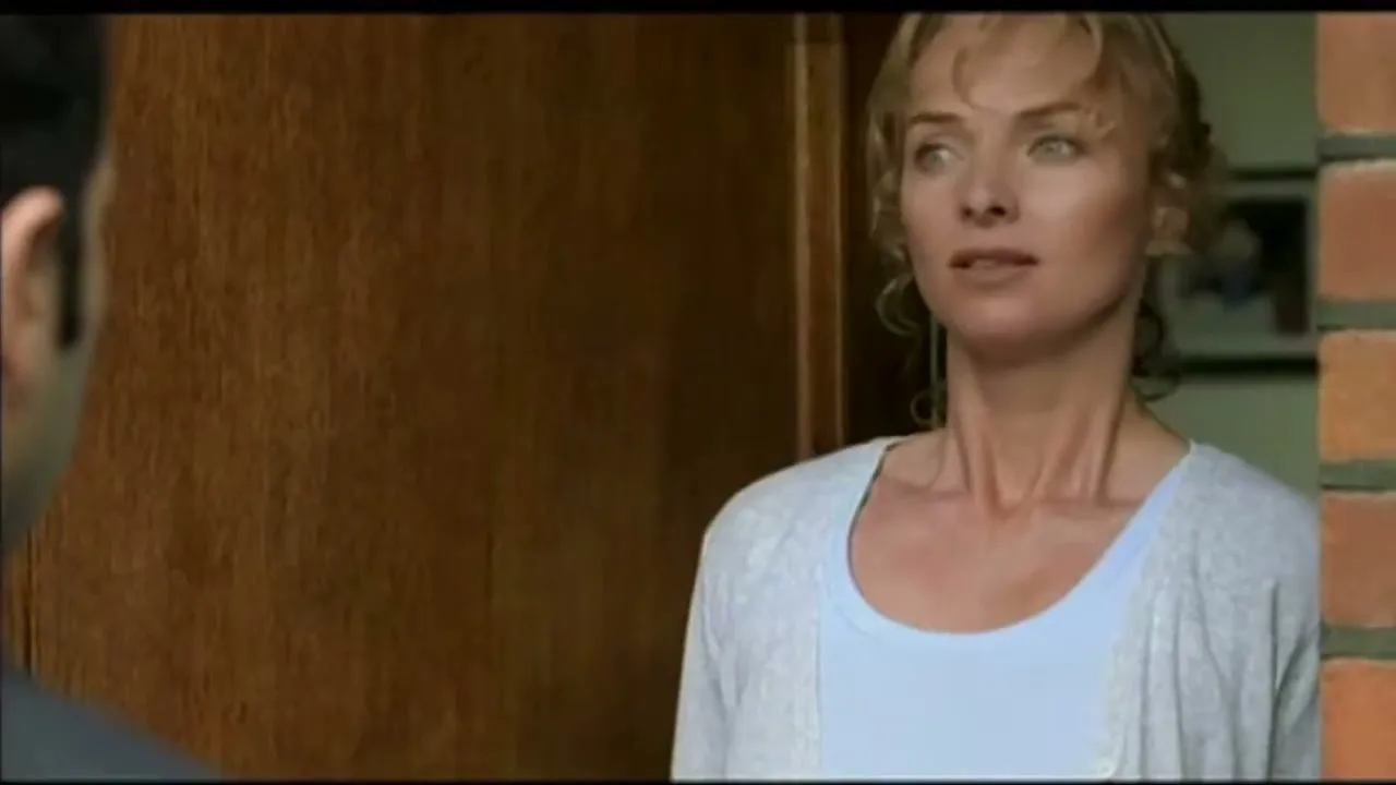 A woman with blonde hair and a light blue top looks concerned while talking to a man at a doorway.