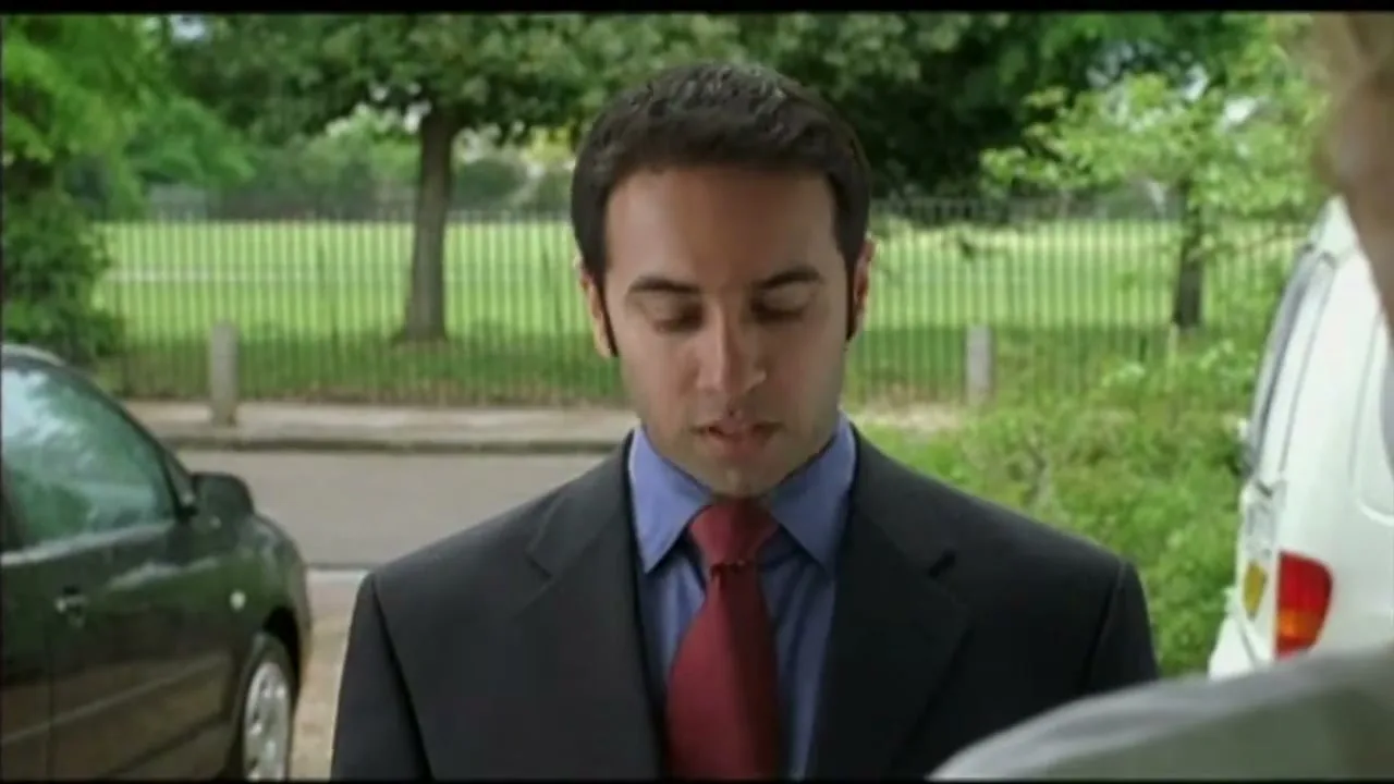 A man in a suit and tie talks to someone off-screen, looking concerned, outdoors during the day.