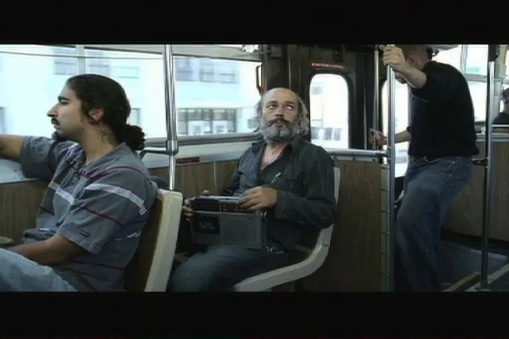 Three men ride a bus, one with a boombox, looking up as if listening to music, in a medium shot.