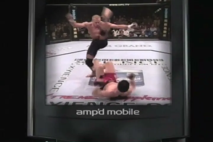 A phone screen displays a UFC fight with one male fighter standing over another on the ground, as the Amp'd Mobile logo appears below.