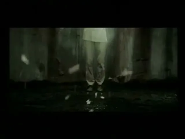A person's legs and feet are seen from the knees down, standing on a dark, wet surface as white debris falls around them in a dark, confined space.