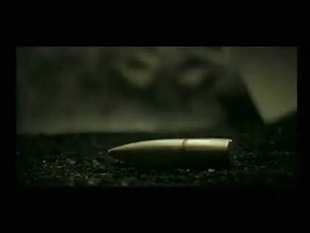 A bullet casing falls and rolls on a dark, gritty surface, with smoke or dust in the background, creating a tense atmosphere.