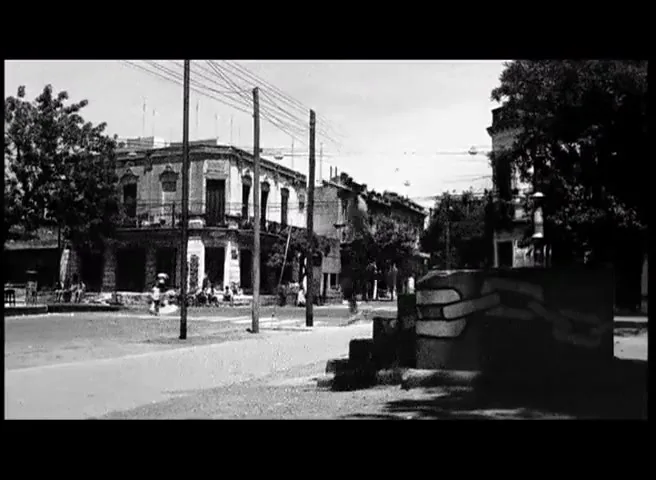 A young boy stands on a stack of books, then jumps off and runs down a street in a black and white, old-fashioned town square.