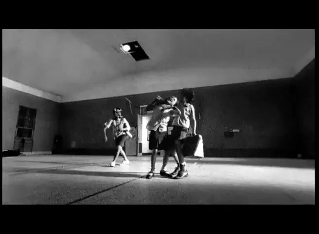 Three children, two girls and a boy, play together in a large, empty room, with one girl running and the other two interacting.