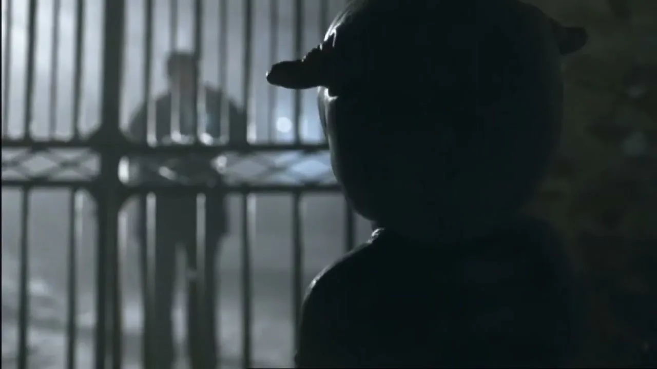 A silhouetted alien creature with horns stands in the foreground, looking towards a blurry figure holding a flashlight behind metal bars.