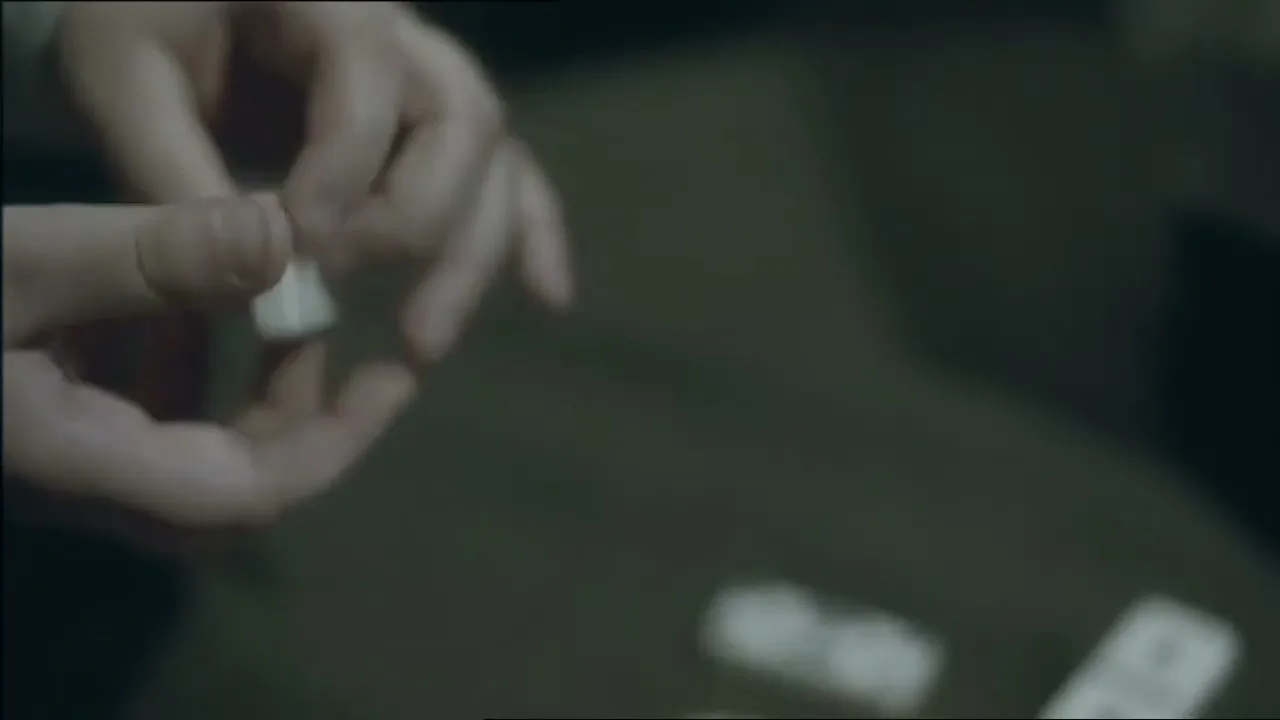 A person's hands hold and manipulate a small, white, rectangular object, possibly a domino, in a dimly lit interior setting.