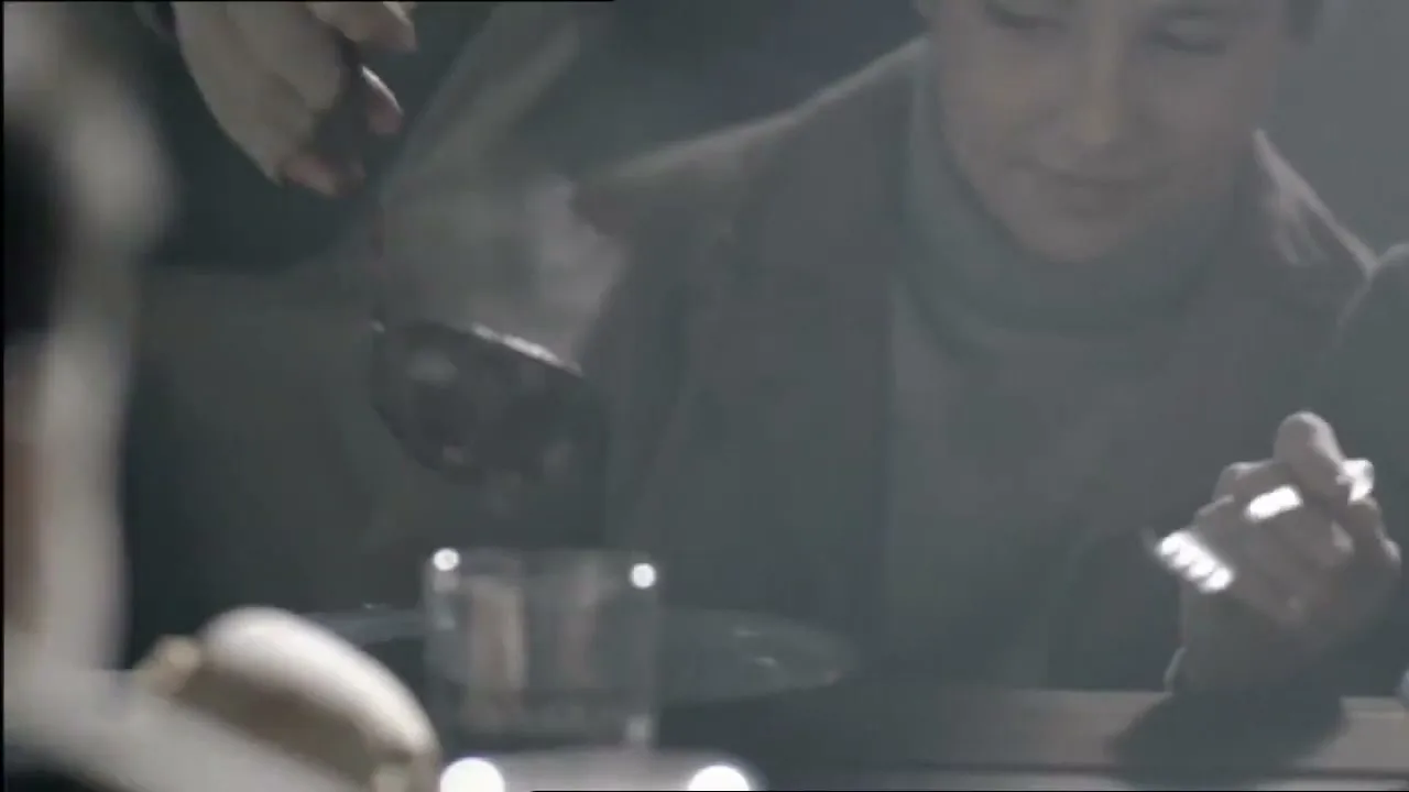 A young person in a turtleneck and coat watches as a hand serves them steaming food from a ladle at a table.