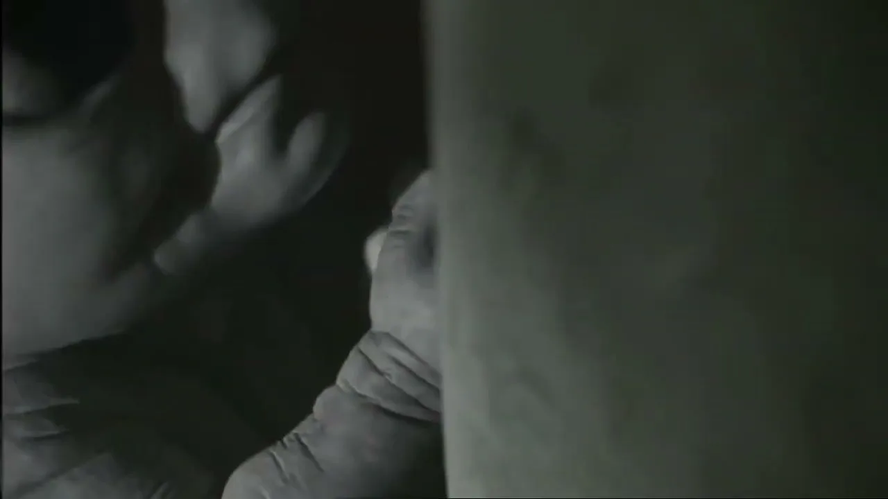 A grey alien with large eyes and wrinkled skin peeks from behind a wall in a dark, mysterious setting.