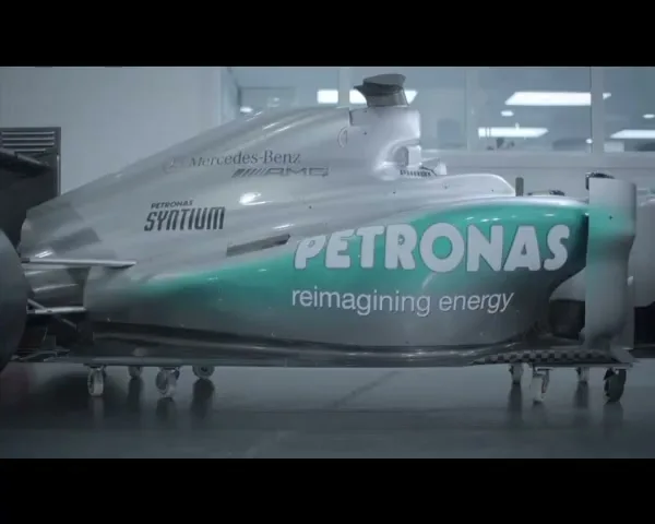 A silver Formula 1 race car chassis with green Petronas branding is seen in a brightly lit workshop.