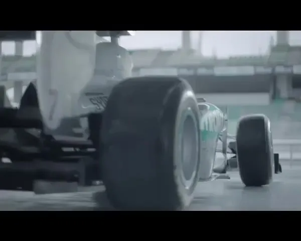 A Formula 1 race car, white with green accents, speeds away from the camera on a wet race track, creating a spray of water.
