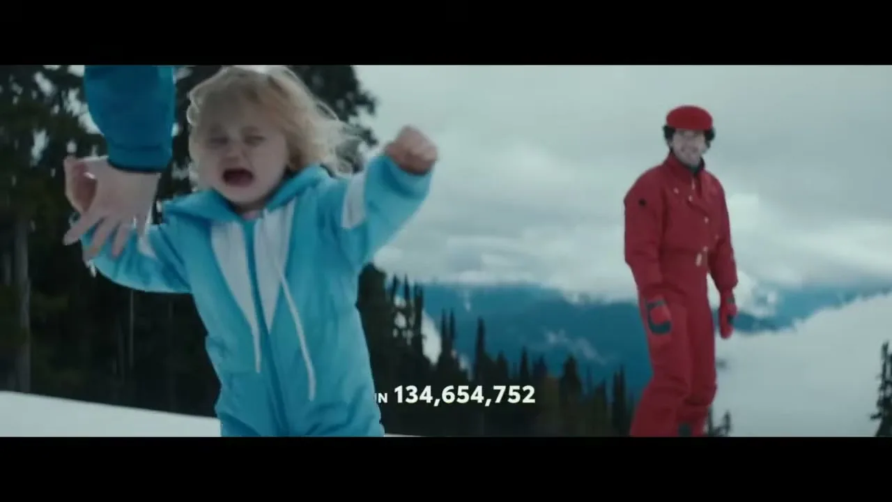 A young child in a blue snowsuit cries and reaches out while being held by an adult's hand, with a man in a red snowsuit standing nearby on a snowy mountain.