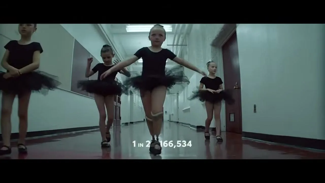 Four young girls in black ballet outfits walk down a school hallway, with the central girl having prosthetic legs, as numbers count down on screen.