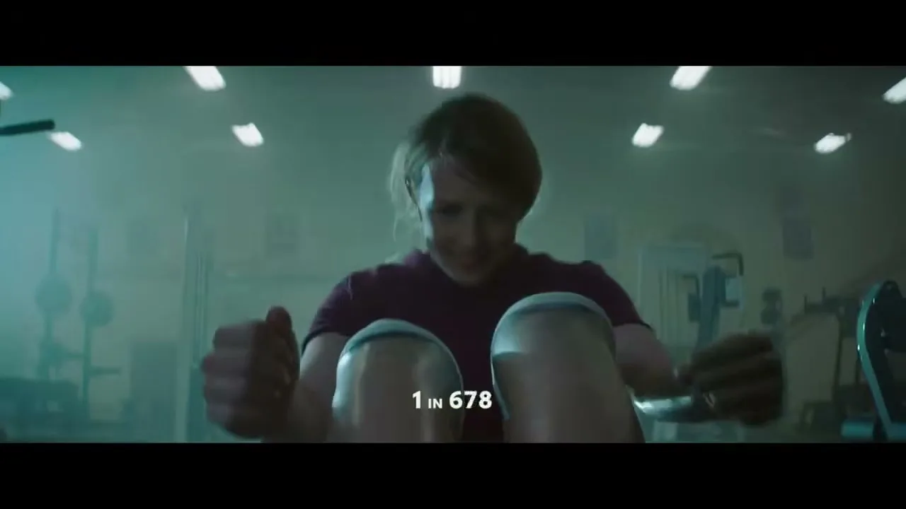 A determined female athlete with short hair rows on a machine in a dimly lit gym, with "1 IN 700" text on screen.