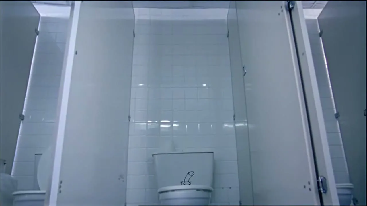 A low-angle shot of a white toilet in a public restroom stall, with a crude drawing on the toilet lid.