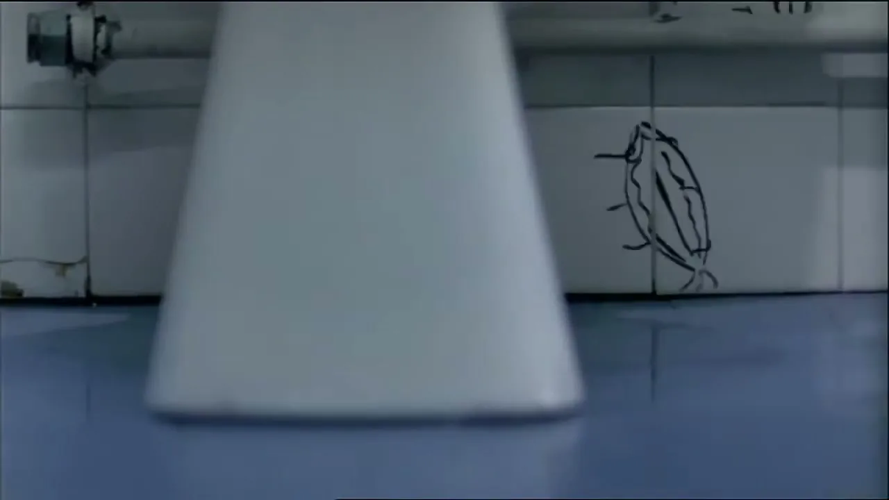 A low-angle shot reveals a crude penis drawing on a tiled wall, partially obscured by a toilet, as the camera pans right to reveal more graffiti.