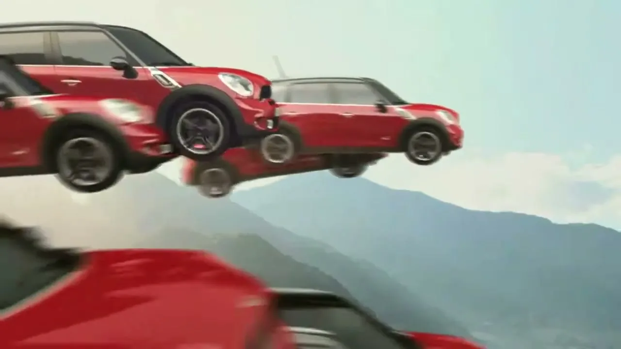 Multiple red Mini Countryman cars appear to be driving in mid-air, forming a diagonal line against a backdrop of mountains and a clear sky.