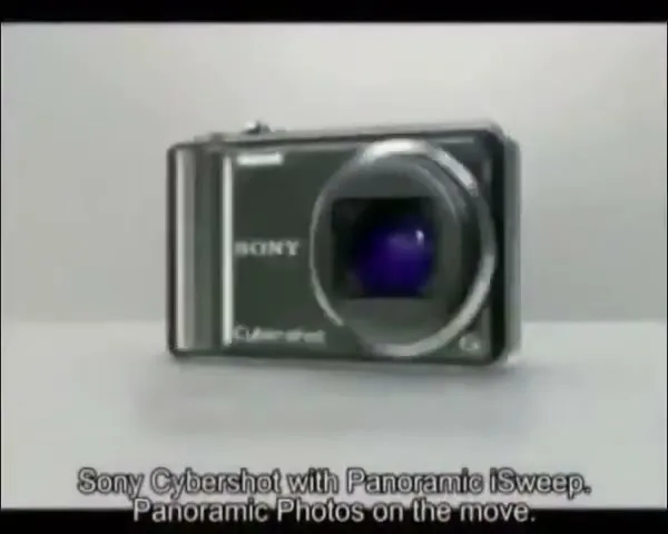 A black Sony Cybershot camera is shown on a white surface, demonstrating its panoramic photo feature with a black and white image on its screen.
