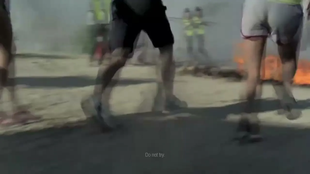 A group of athletes run past a wall of fire on a sandy track, with "Do not try." text on screen.
