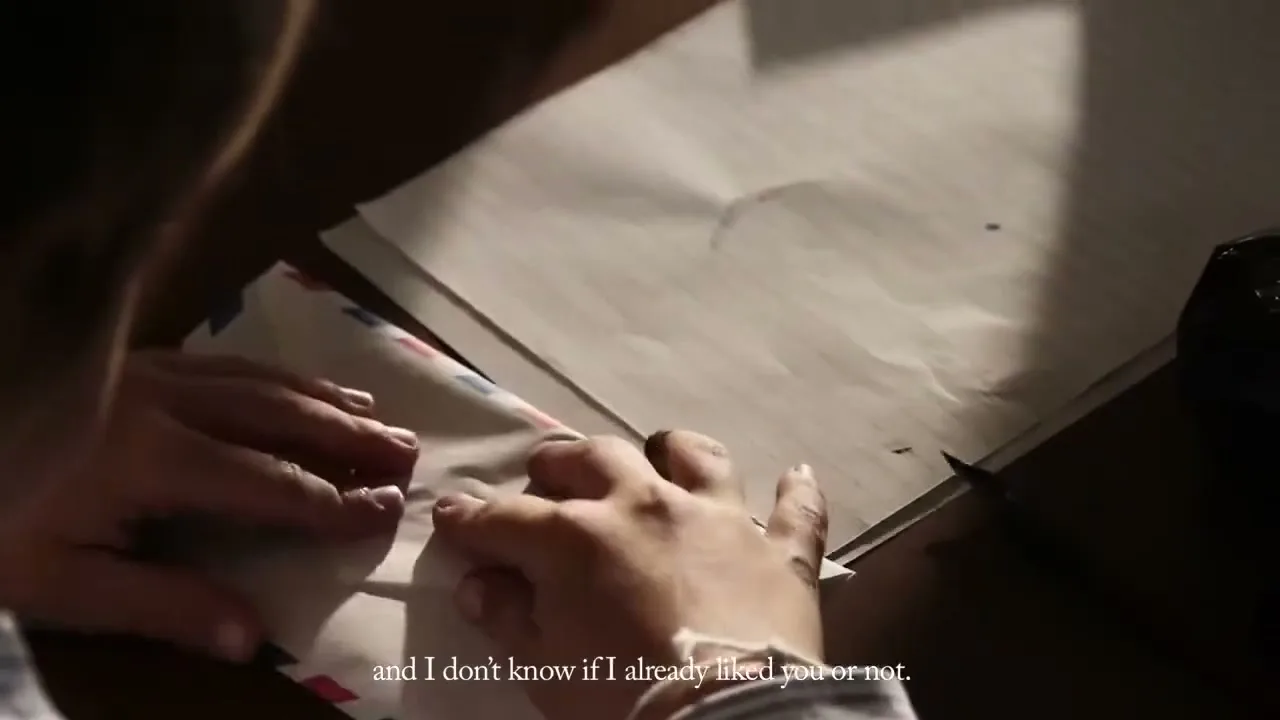 A young person's hands are seen from above, carefully folding a letter into an airmail envelope on a wooden desk.