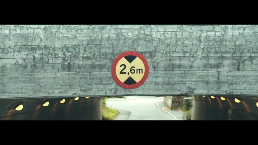 A yellow and red circular sign with "2,6m" in black text is centered on a concrete bridge over a road and tunnel.