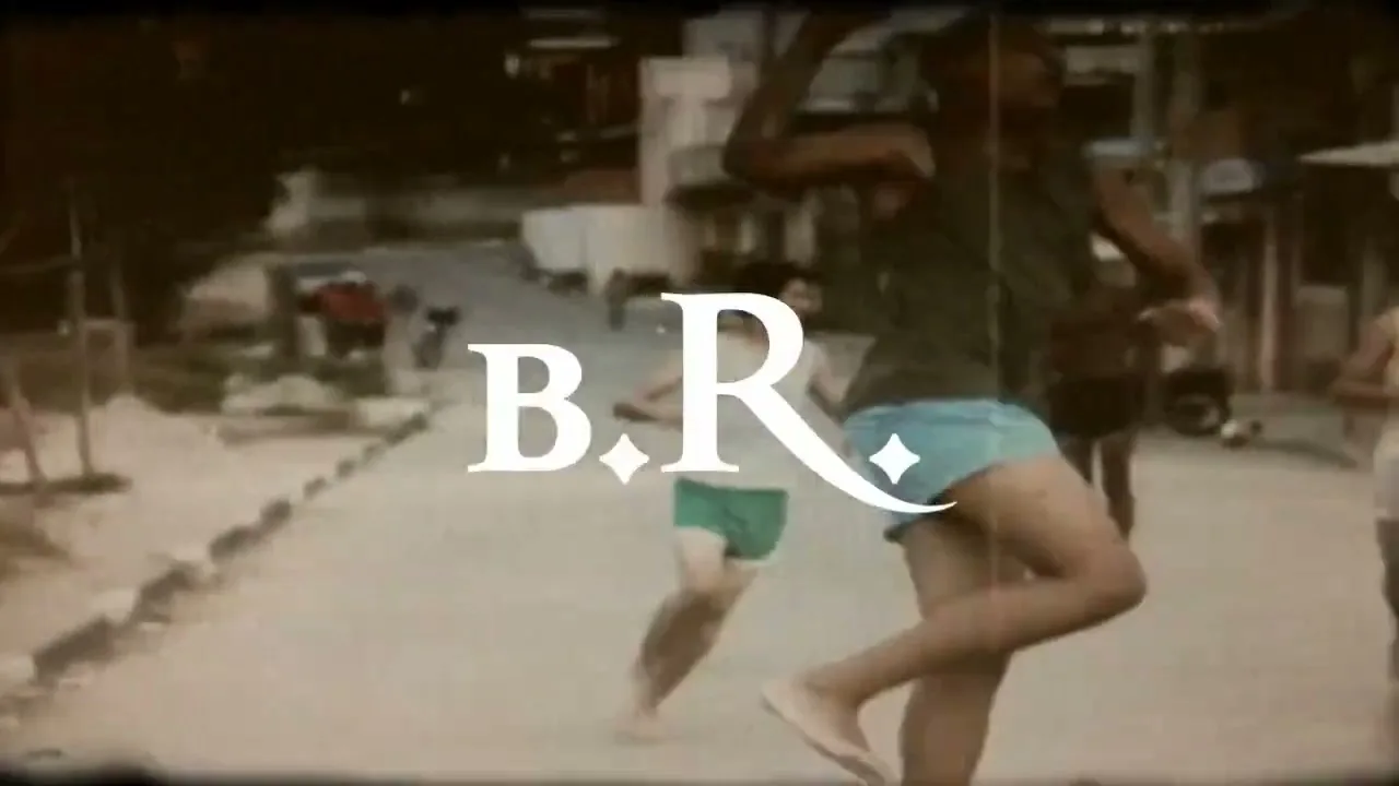 A young male athlete in a tank top and shorts jumps and kicks in a blurry, vintage-style shot on a street with other people in the background.