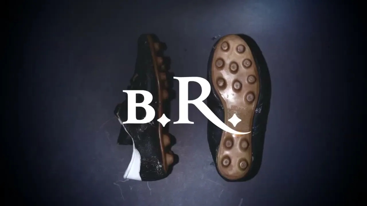 A pair of old, worn-out black soccer cleats with brown studs are shown from an overhead perspective on a dark surface, with white text appearing over them.