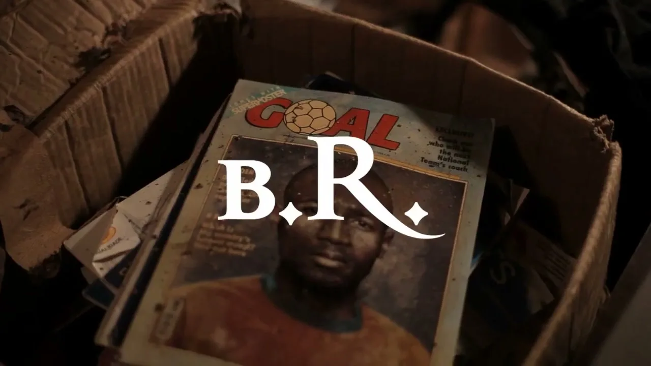 A close-up shot of an old, worn "GOAL" magazine featuring a Black male soccer player on the cover, lying in a cardboard box.