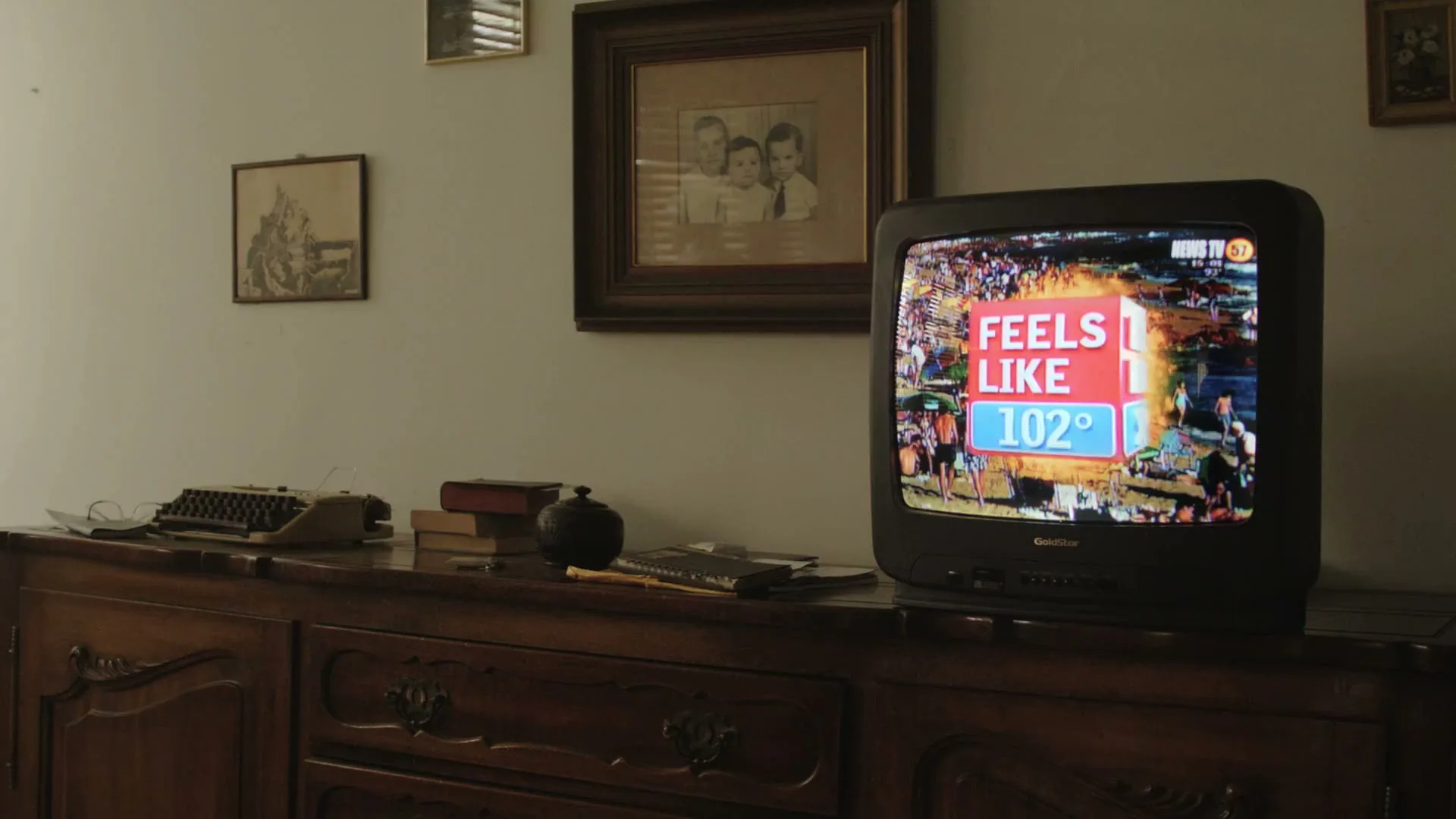 A vintage television set displays a news report about a heatwave, sitting on a wooden cabinet in a dimly lit room.