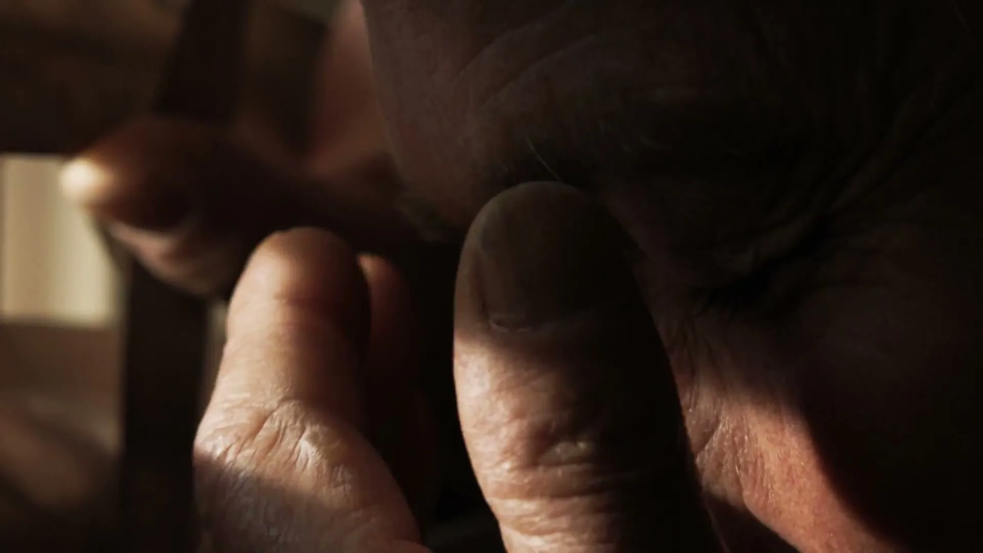 A man's face is shown in extreme closeup, with his fingers touching his nose, as he smells something in a dimly lit interior.