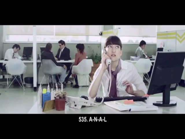 A female office worker with a short bob haircut sits at her desk, talking on the phone and looking frustrated in a bright, modern office.