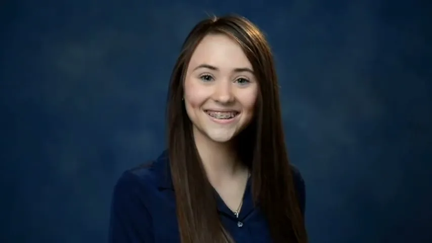 A smiling teen girl with braces and long brown hair poses for a school photo against a blue backdrop.