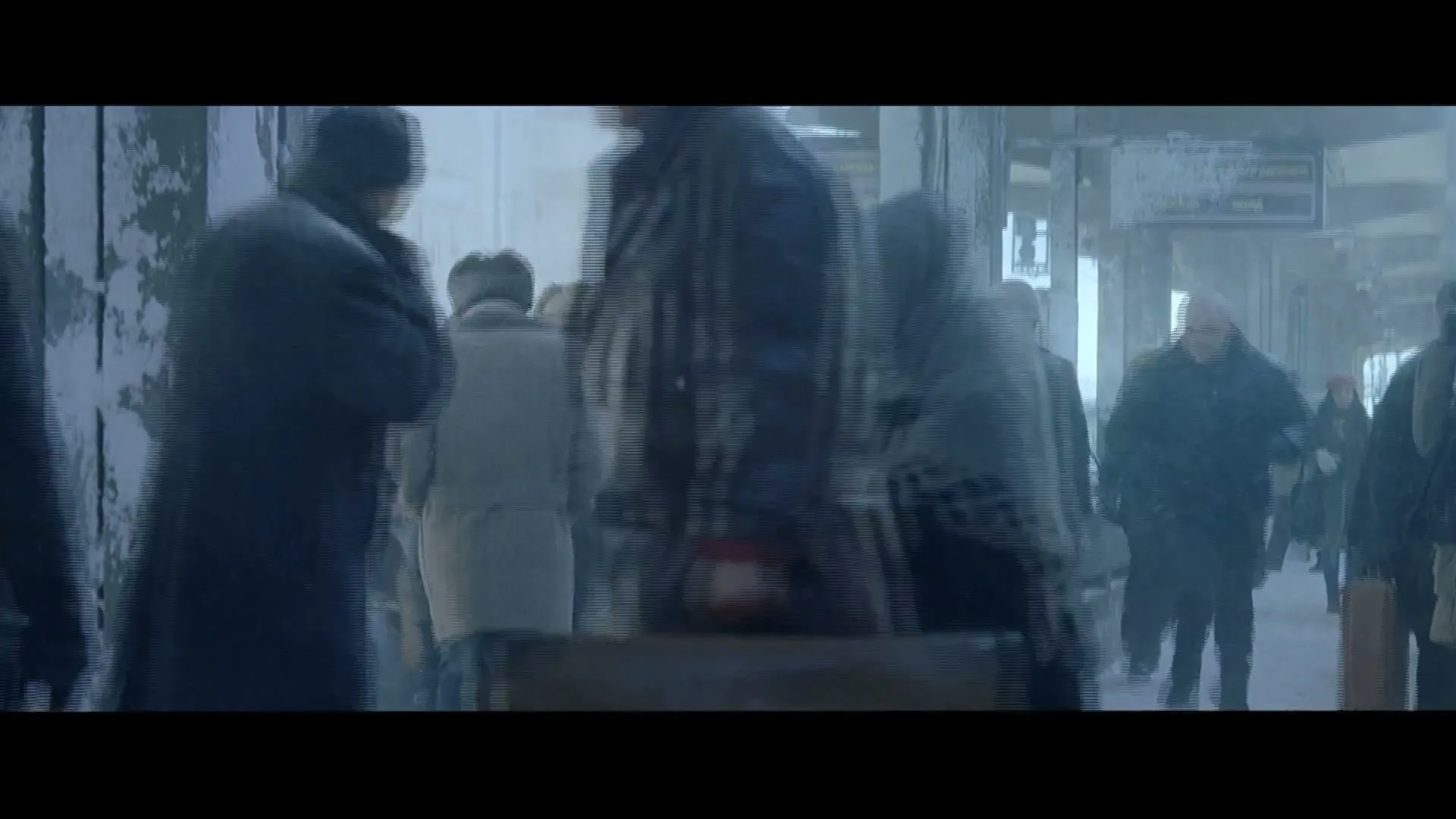 A crowd of people in heavy winter coats walk through a snowy, cold train station platform during a blizzard.