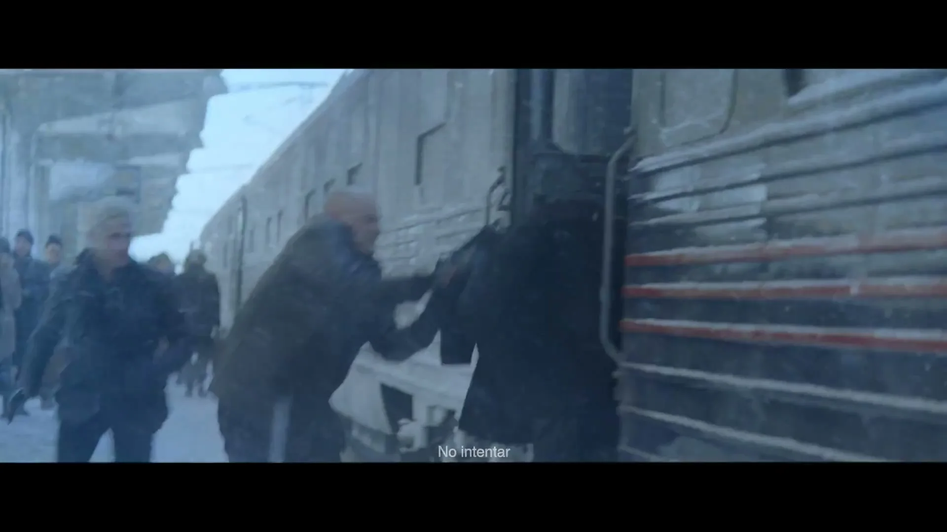 A man in a dark coat is pushed onto a moving train by another man in a dark jacket, while a third person watches on a snowy platform.