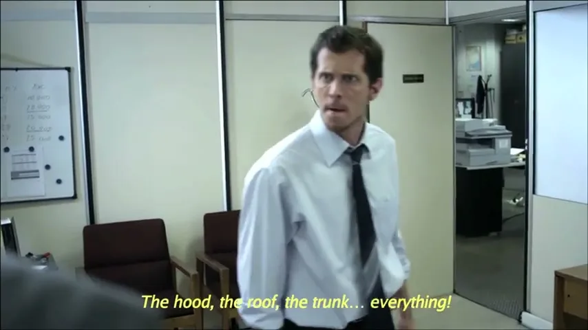 A man in a white shirt and black tie yells at another man, pointing his finger, in an office setting.