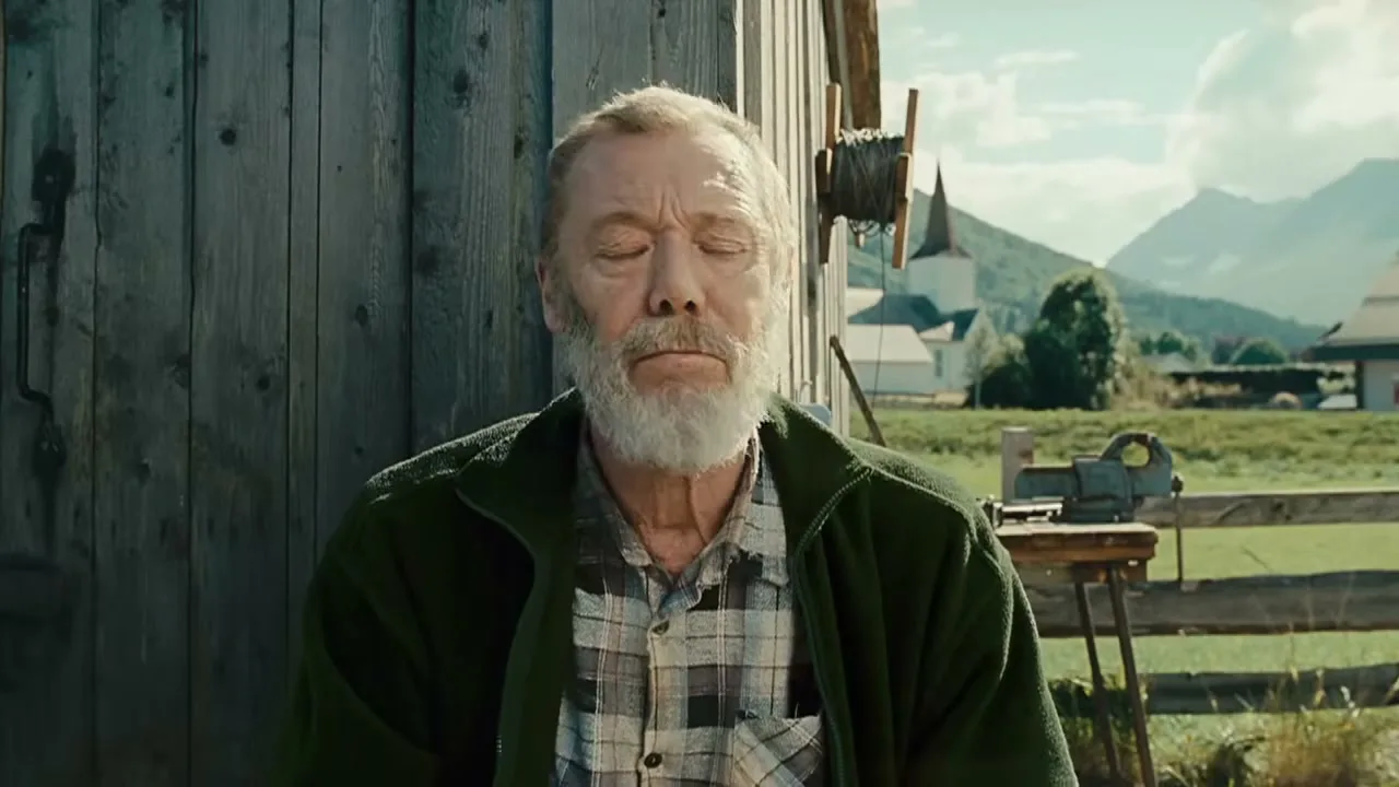 An older man with a white beard and green jacket closes his eyes, then opens them, looking directly at the camera in a rural setting.