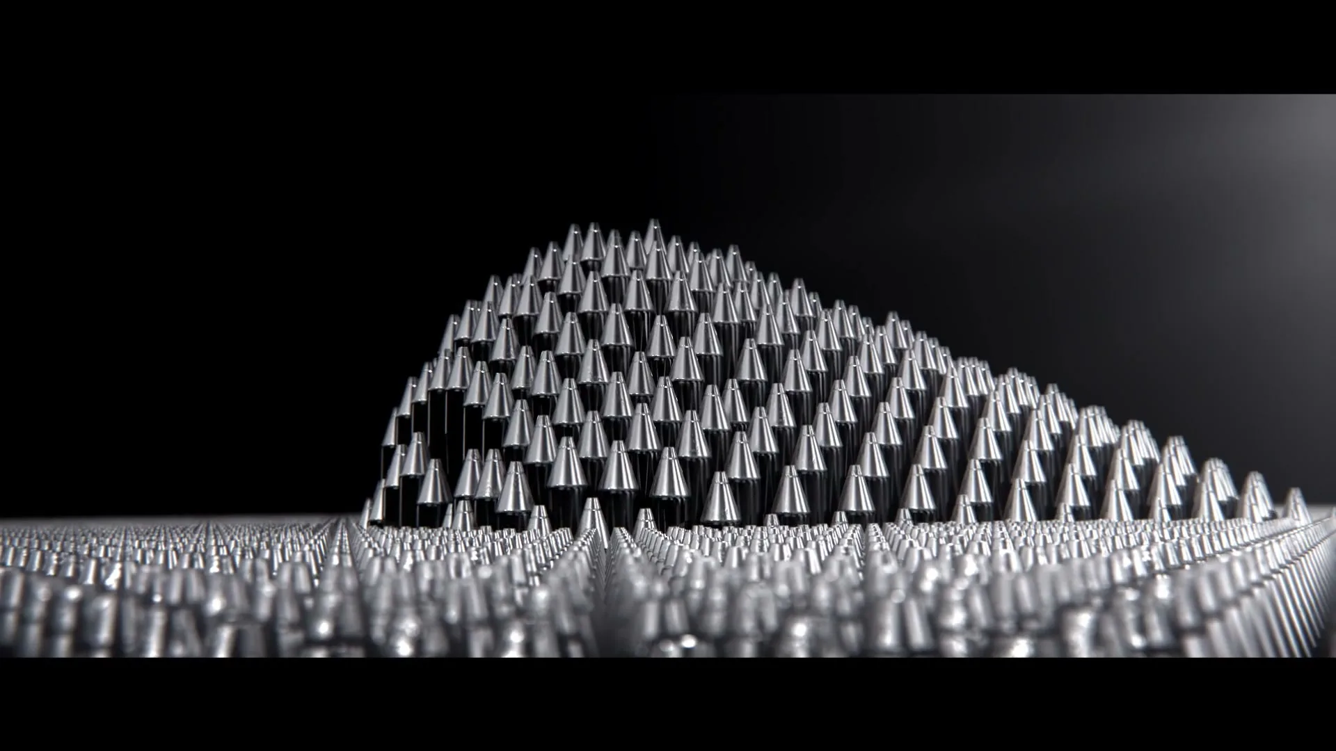 Thousands of silver pen nibs are arranged in a dense, undulating pattern, forming a mountain-like shape against a dark background.