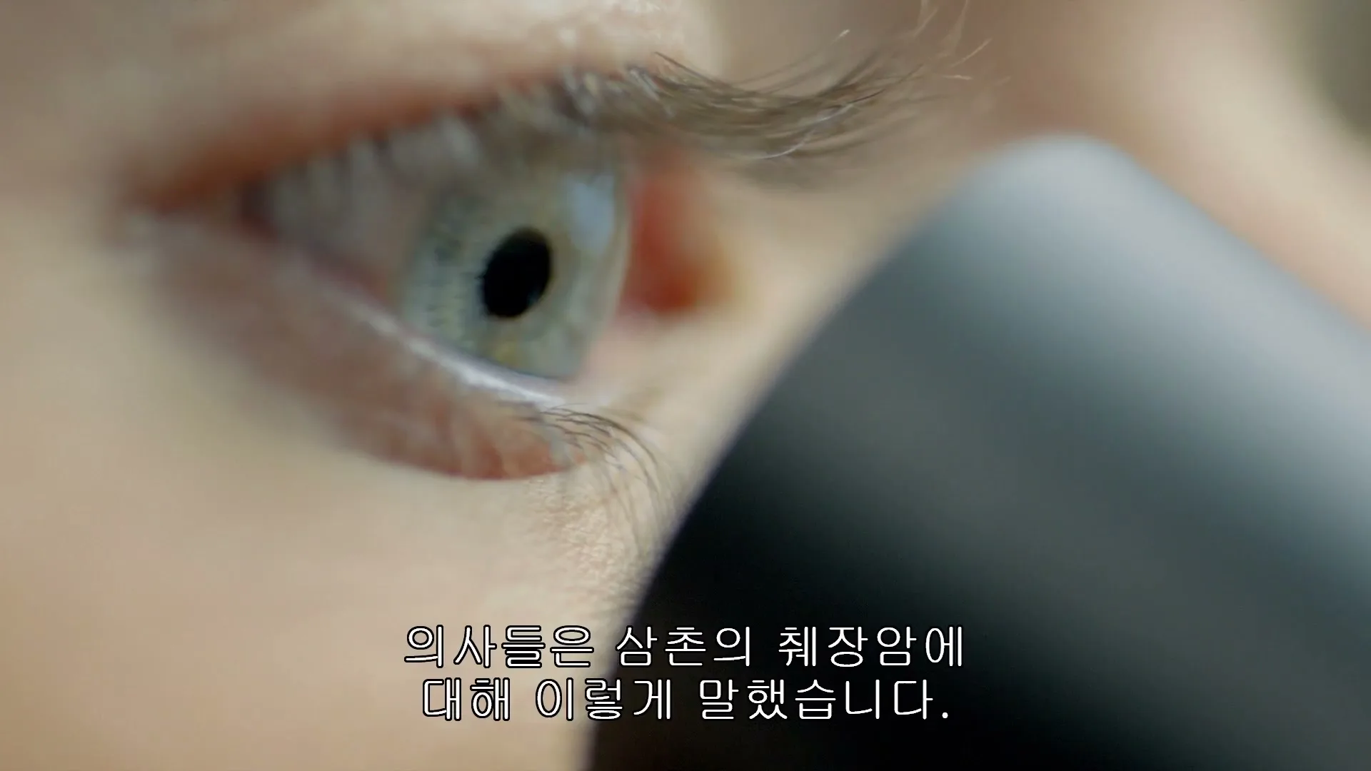 A close-up shot of a person's eye looking into a microscope, with their eyelashes and skin visible.