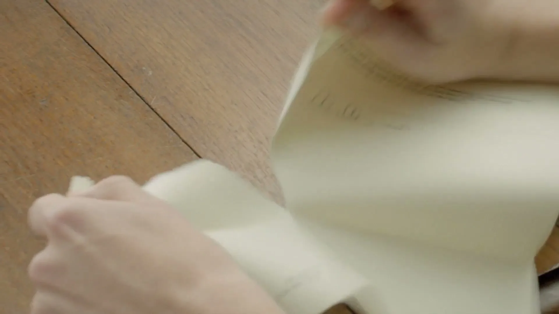 A person's hands are seen from above, tearing a piece of paper on a wooden table, with a quick, energetic motion.