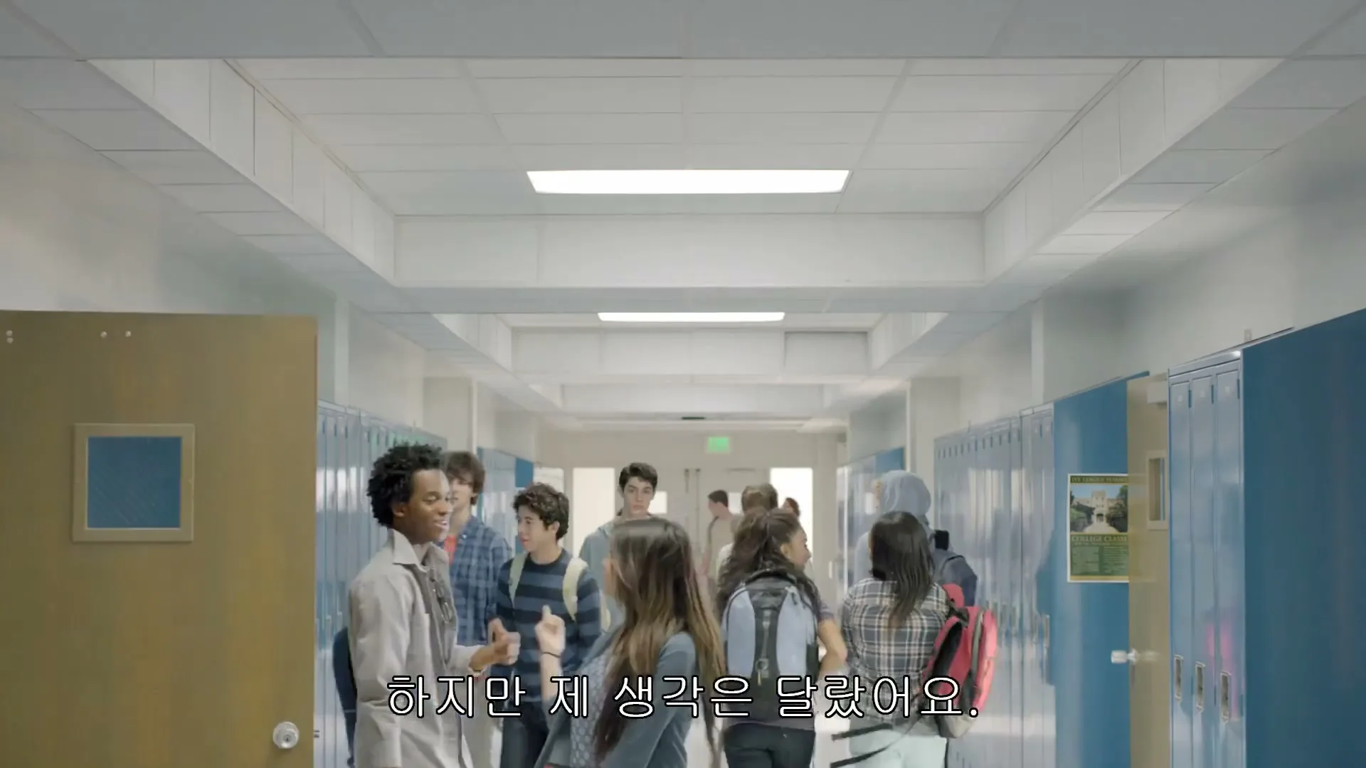 A diverse group of high school students walks down a brightly lit hallway with blue lockers, some smiling and talking.