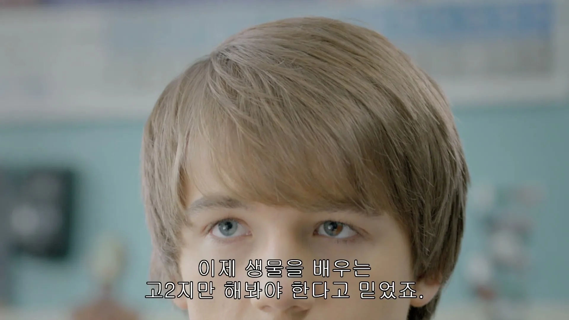 A young male with light brown hair and heterochromia opens his eyes, looking up in a classroom setting.