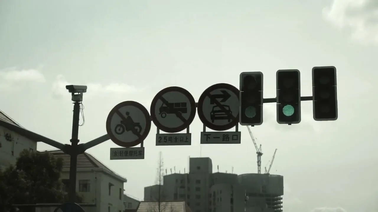 A low-angle shot of a traffic light and three circular traffic signs with Chinese characters, against a cloudy sky and buildings in the background.